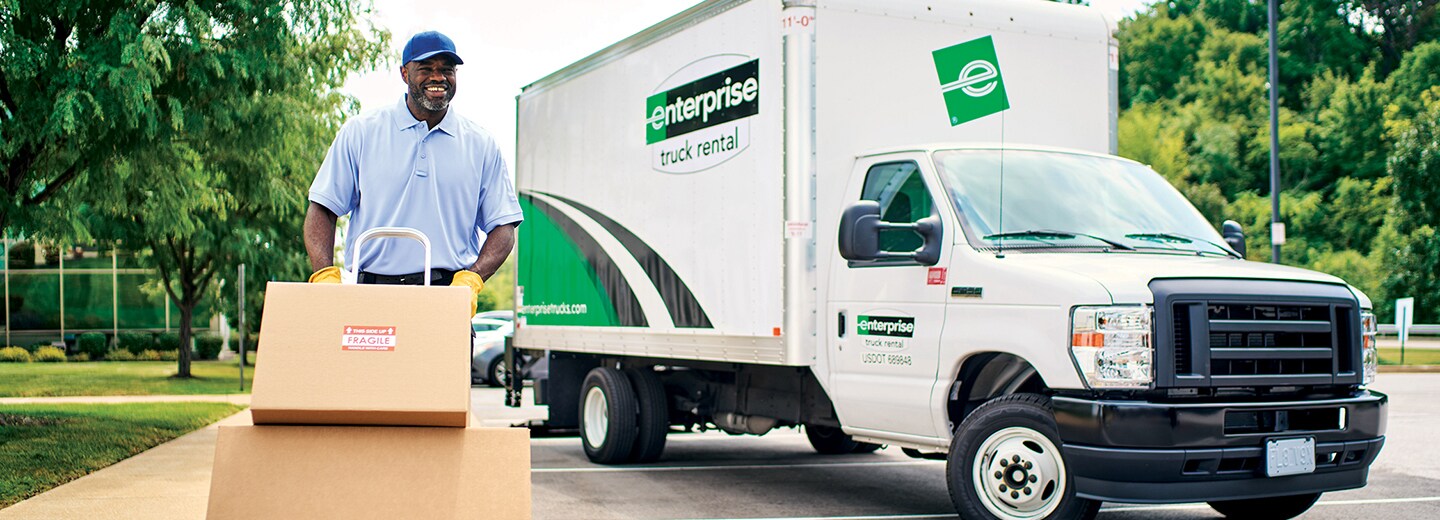 Man pushing boxes on a hand truck in front of an Enterprise Parcel Van